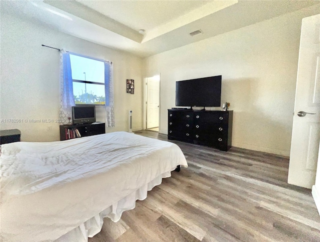 bedroom with a raised ceiling, wood finished floors, and visible vents