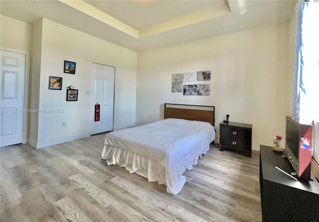 bedroom featuring baseboards, a raised ceiling, and light wood-style flooring