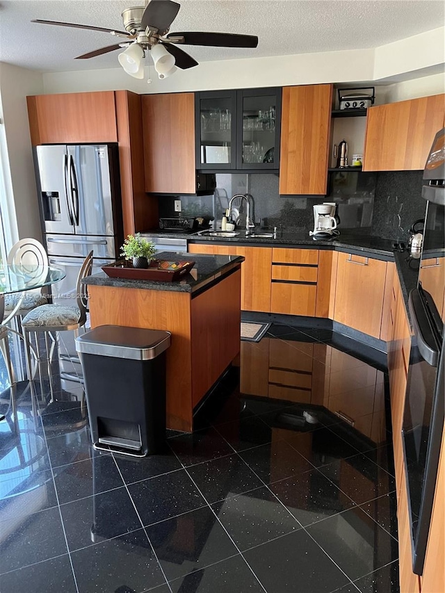 kitchen with dark countertops, tasteful backsplash, stainless steel fridge with ice dispenser, granite finish floor, and a sink