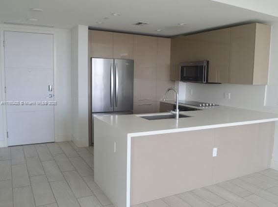 kitchen featuring visible vents, a sink, appliances with stainless steel finishes, a peninsula, and light countertops