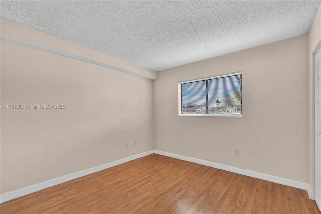 unfurnished room with a textured ceiling, light wood-type flooring, and baseboards