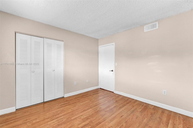 unfurnished bedroom featuring baseboards, visible vents, a closet, a textured ceiling, and light wood-type flooring