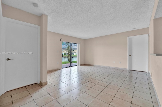 spare room featuring light tile patterned floors, a textured ceiling, and baseboards