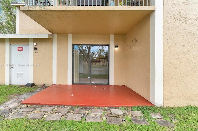 view of exterior entry with a balcony and stucco siding