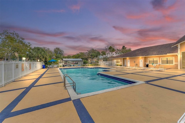 pool at dusk with a patio area, a community pool, and fence