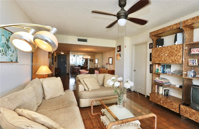 living area with visible vents, a textured ceiling, and ceiling fan with notable chandelier