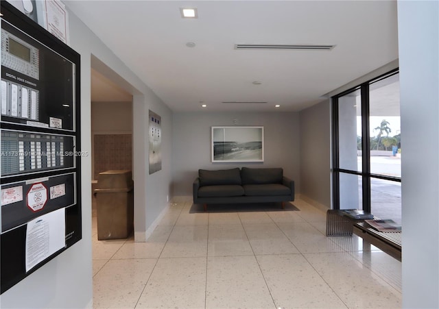hallway featuring light speckled floor, baseboards, a wall of windows, and visible vents