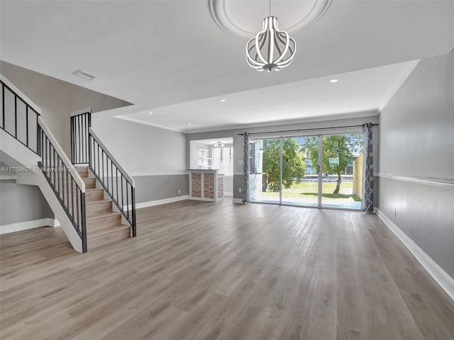 unfurnished living room with ornamental molding, wood finished floors, baseboards, a chandelier, and stairs