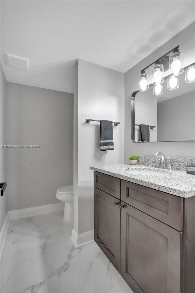 bathroom with marble finish floor, toilet, vanity, and baseboards