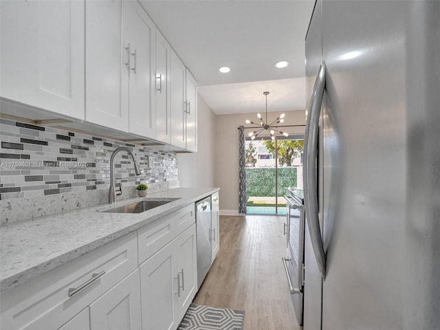 kitchen featuring a sink, tasteful backsplash, white cabinetry, light wood-style floors, and appliances with stainless steel finishes