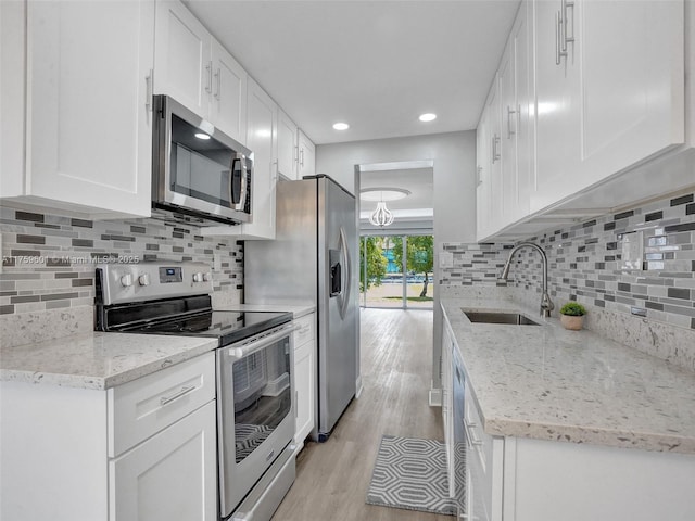 kitchen featuring a sink, light wood-style floors, appliances with stainless steel finishes, white cabinetry, and backsplash