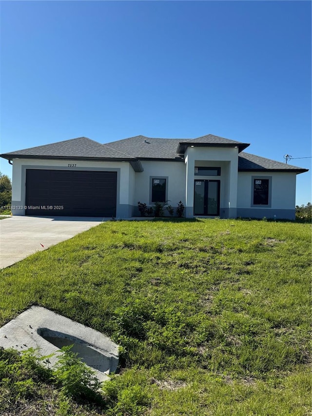 prairie-style house with a front lawn, concrete driveway, roof with shingles, stucco siding, and an attached garage