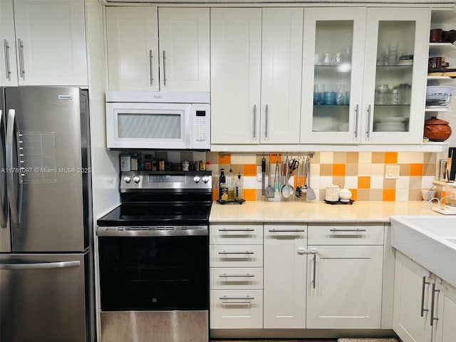 kitchen featuring white microwave, tasteful backsplash, freestanding refrigerator, electric stove, and white cabinetry