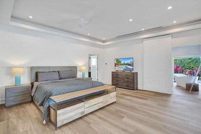 bedroom with recessed lighting, a raised ceiling, and light wood-style floors