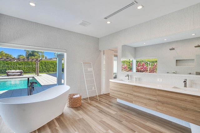 bathroom featuring a wealth of natural light, a freestanding bath, wood finished floors, and a sink