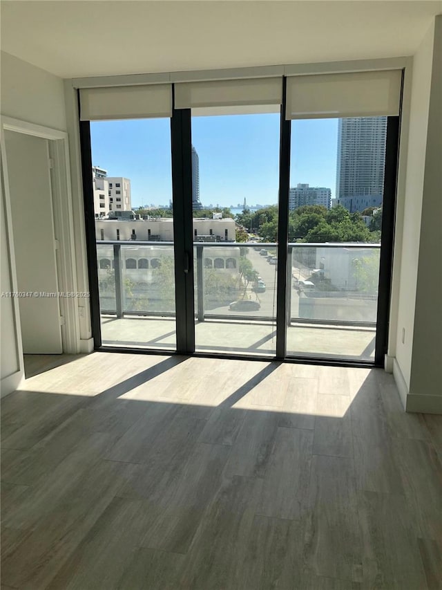 unfurnished room with a city view, a wall of windows, and wood finished floors