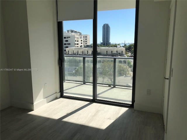 empty room with expansive windows, baseboards, a city view, and wood finished floors