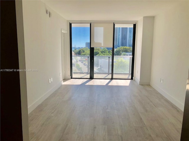 spare room with a wall of windows, baseboards, and wood finished floors