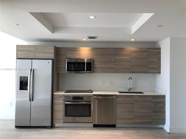 kitchen featuring a sink, light countertops, appliances with stainless steel finishes, a raised ceiling, and modern cabinets