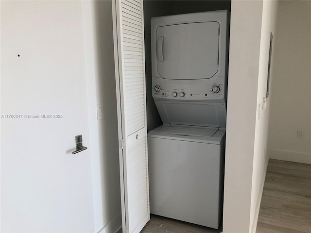 laundry area featuring laundry area, stacked washer and dryer, wood finished floors, and baseboards