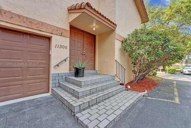 property entrance with stucco siding, a tiled roof, and a garage