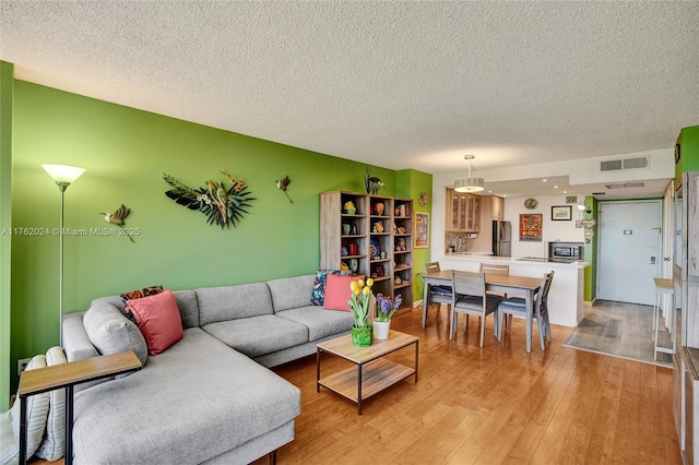 living area featuring light wood-type flooring, visible vents, and a textured ceiling