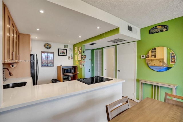 kitchen with a peninsula, freestanding refrigerator, a sink, stainless steel microwave, and black electric stovetop