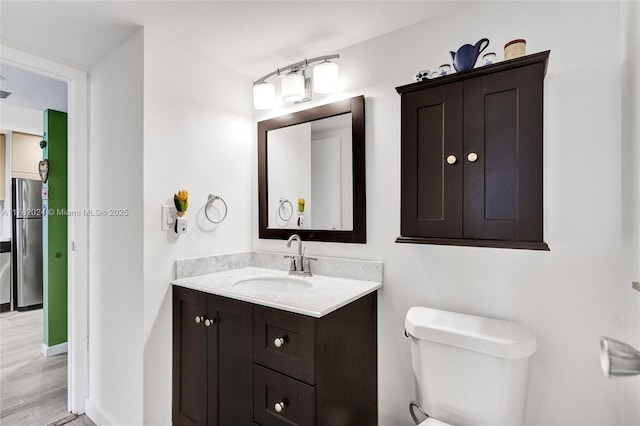 bathroom with vanity, toilet, wood finished floors, and baseboards