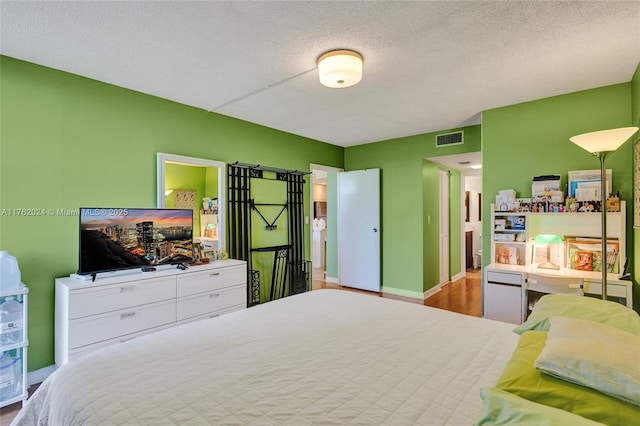 bedroom featuring visible vents, baseboards, a textured ceiling, and wood finished floors