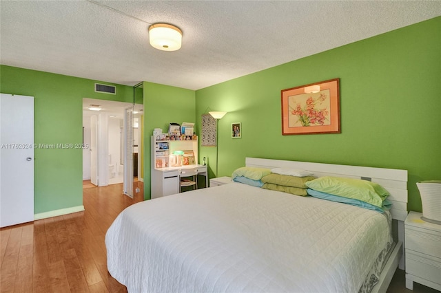 bedroom featuring visible vents, a textured ceiling, baseboards, and hardwood / wood-style flooring