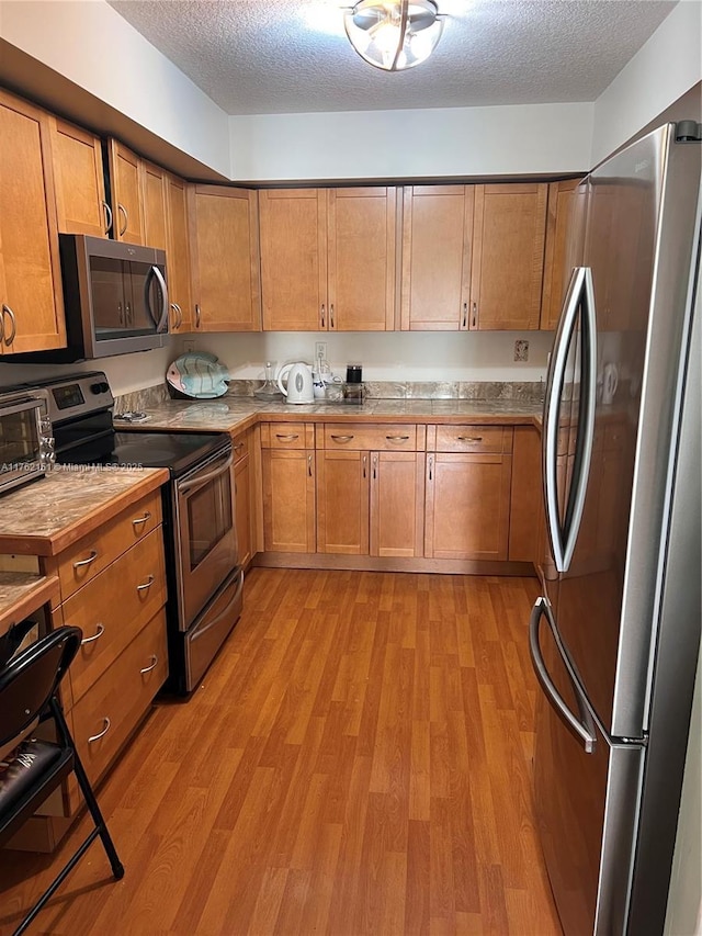 kitchen featuring light wood finished floors, appliances with stainless steel finishes, and a textured ceiling