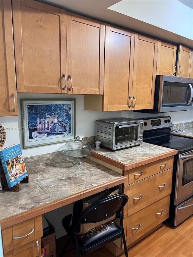 kitchen with tile countertops, appliances with stainless steel finishes, light wood-style flooring, and a toaster