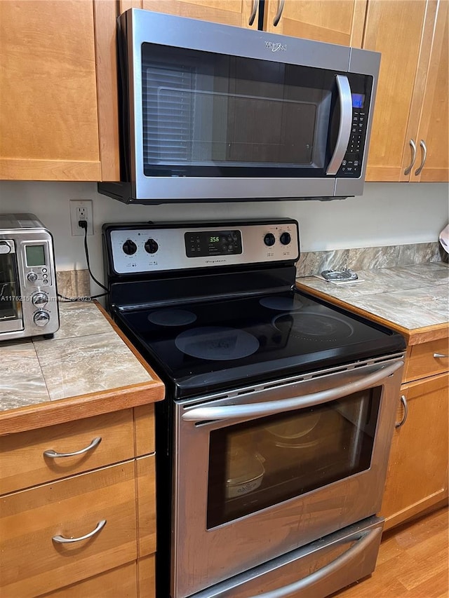 kitchen featuring tile countertops, appliances with stainless steel finishes, and light wood finished floors