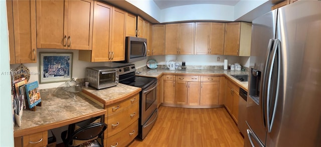 kitchen featuring brown cabinetry, a toaster, stainless steel appliances, tile counters, and light wood-type flooring