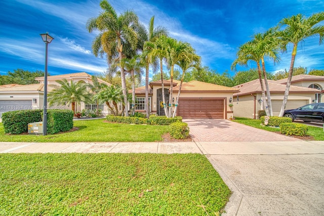 view of front of home featuring a front lawn, a tiled roof, stucco siding, decorative driveway, and a garage