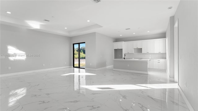 unfurnished living room featuring recessed lighting, a raised ceiling, baseboards, and a sink