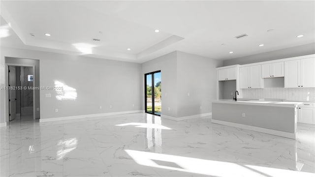 kitchen featuring marble finish floor, a kitchen island with sink, a tray ceiling, tasteful backsplash, and recessed lighting