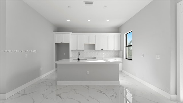 kitchen featuring visible vents, backsplash, baseboards, an island with sink, and a sink