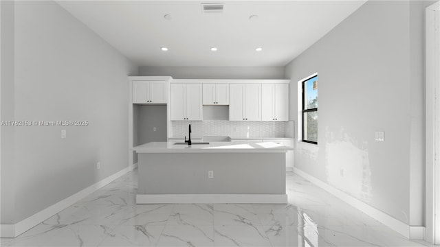 kitchen featuring a kitchen island with sink, visible vents, decorative backsplash, white cabinets, and a sink