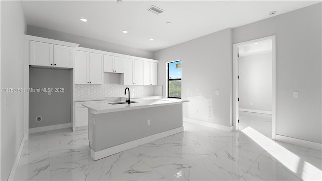 kitchen with visible vents, backsplash, a center island with sink, marble finish floor, and a sink