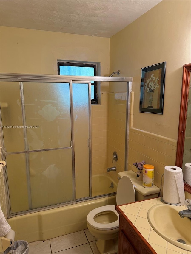 full bathroom featuring toilet, combined bath / shower with glass door, tile walls, tile patterned flooring, and vanity