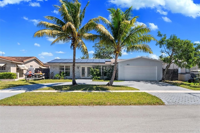 ranch-style home featuring an attached garage, a front lawn, french doors, decorative driveway, and roof mounted solar panels