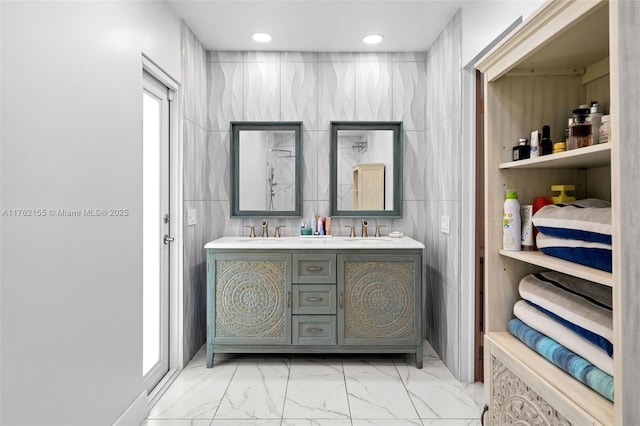 bathroom featuring a sink, tile walls, marble finish floor, and double vanity