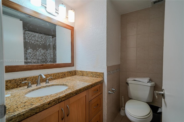 bathroom with visible vents, toilet, vanity, and a textured wall