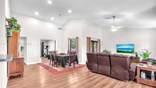 living area with light wood-type flooring, a textured ceiling, ceiling fan, and high vaulted ceiling