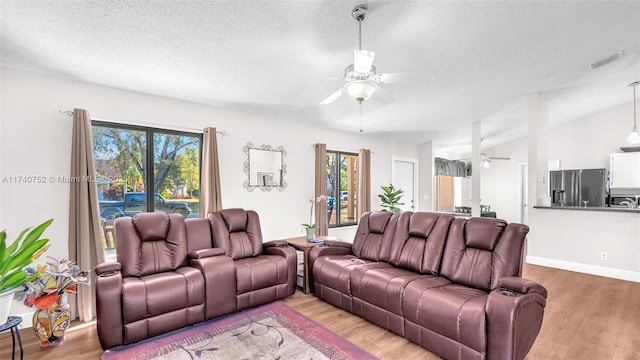 living area with visible vents, vaulted ceiling, wood finished floors, a textured ceiling, and a ceiling fan