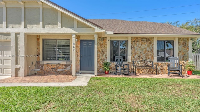 doorway to property featuring stone siding, a lawn, a shingled roof, and stucco siding