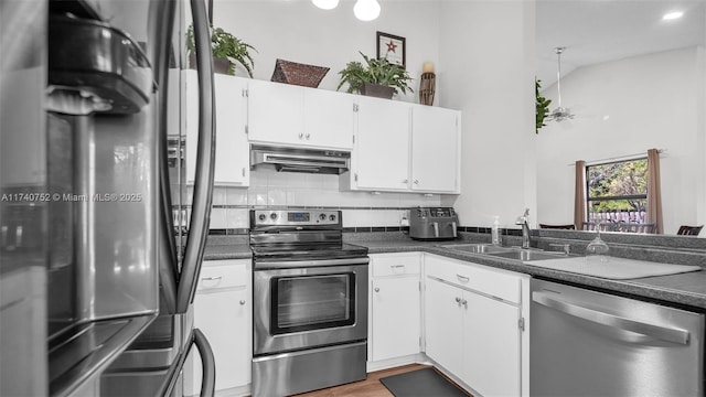 kitchen with a sink, stainless steel appliances, under cabinet range hood, dark countertops, and backsplash