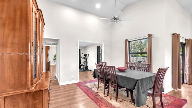 dining space featuring baseboards, light wood-type flooring, a towering ceiling, and ceiling fan