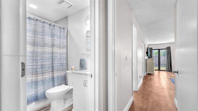 bathroom featuring toilet, vanity, a shower with curtain, wood finished floors, and a textured ceiling